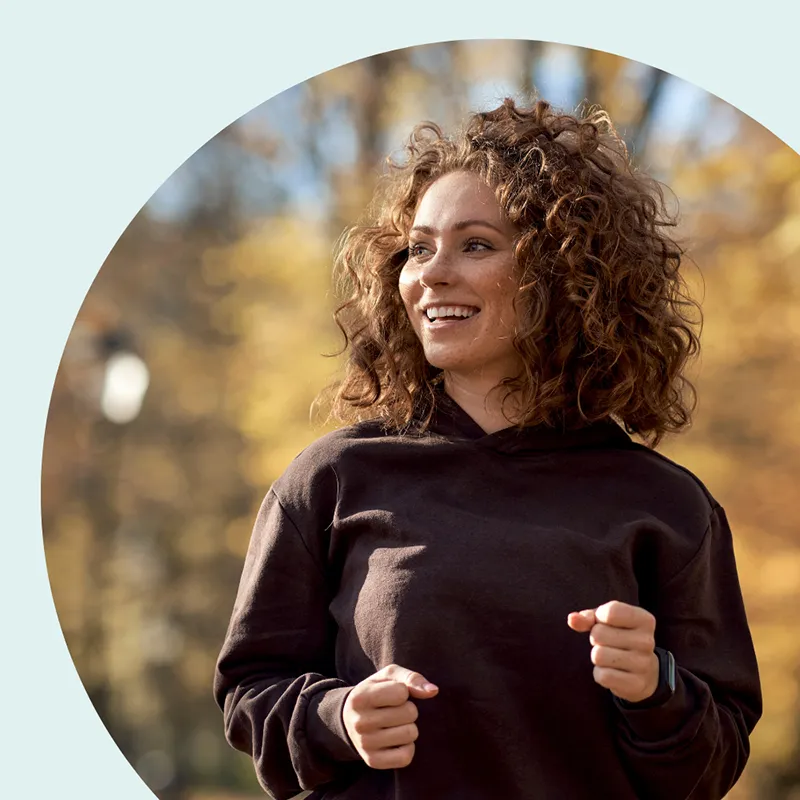 Eine Frau joggt glücklich durch eine herbstliche Landschaft.